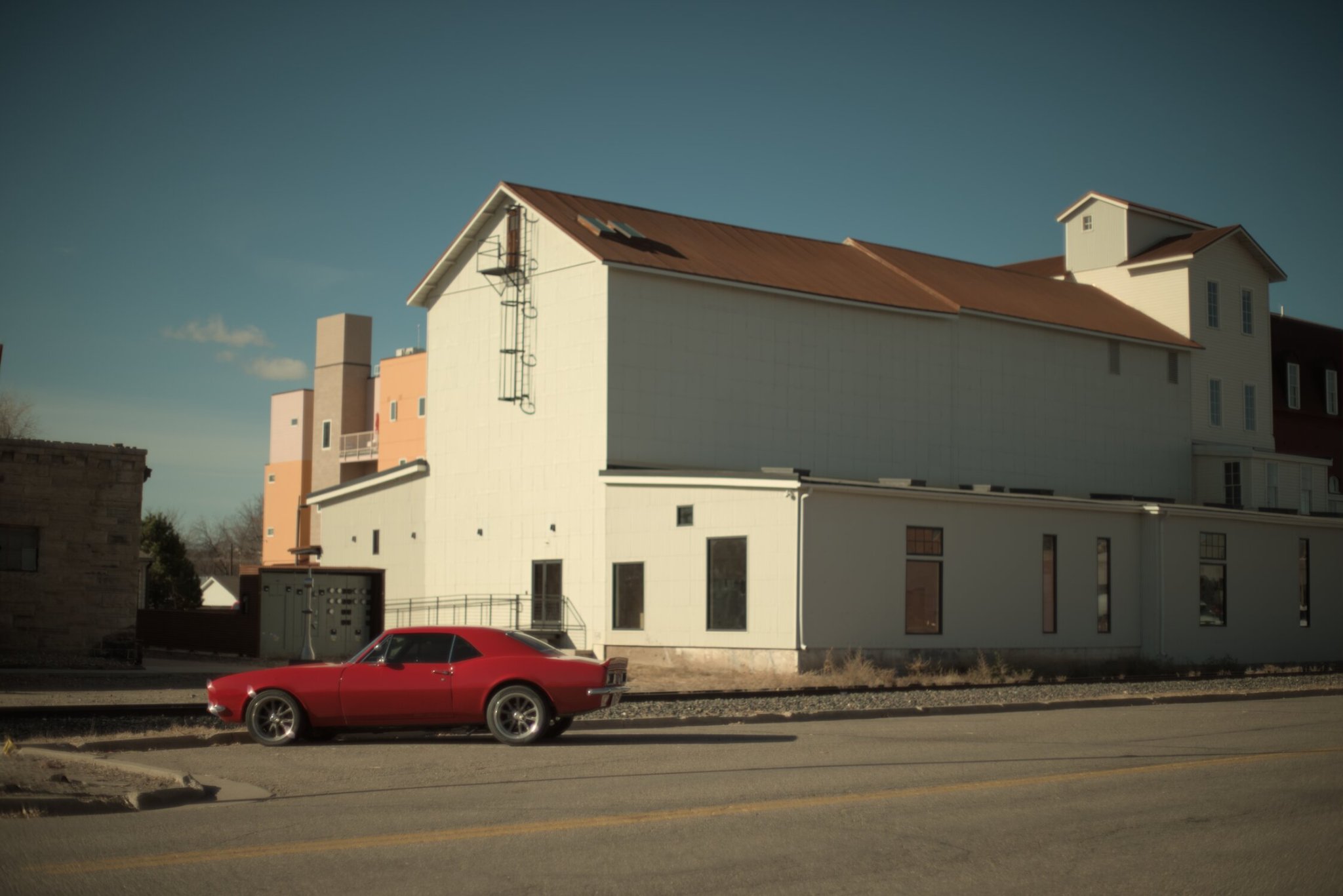 a barn shaped building behind a rail, with a red car in front