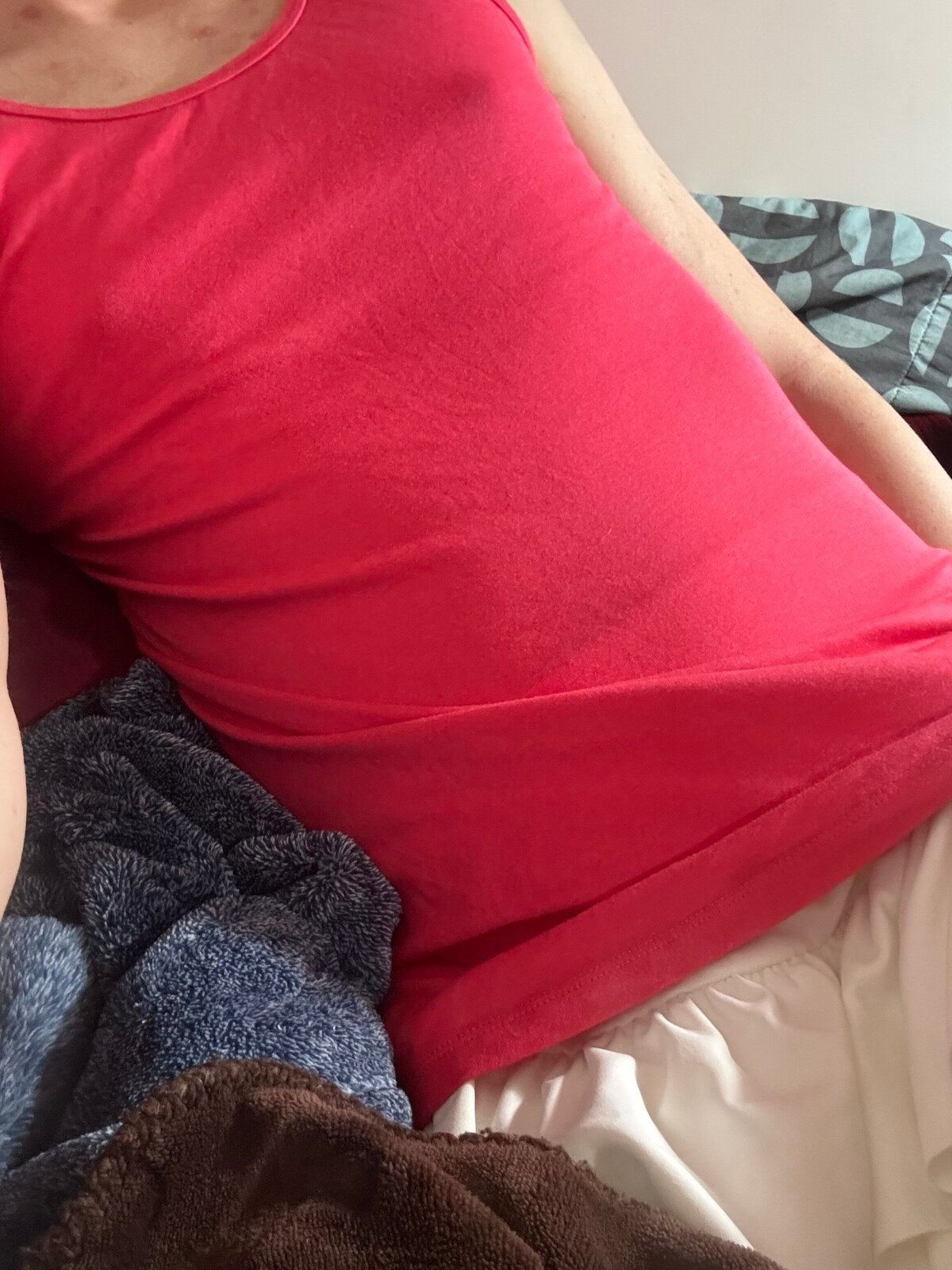 a tidy, chilling in bed, torso visible... wearing a white skirt and pink tank top, nipples are visibly poking through