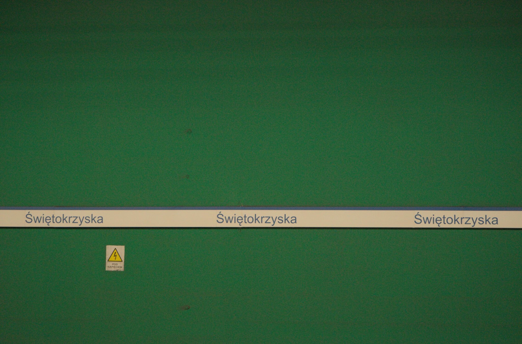 a flat green wall, with a white band containing the station's name, an electric shock warning to the lower left of frame, filled with digital grain, it feels uncomfortable, not an honourable place....