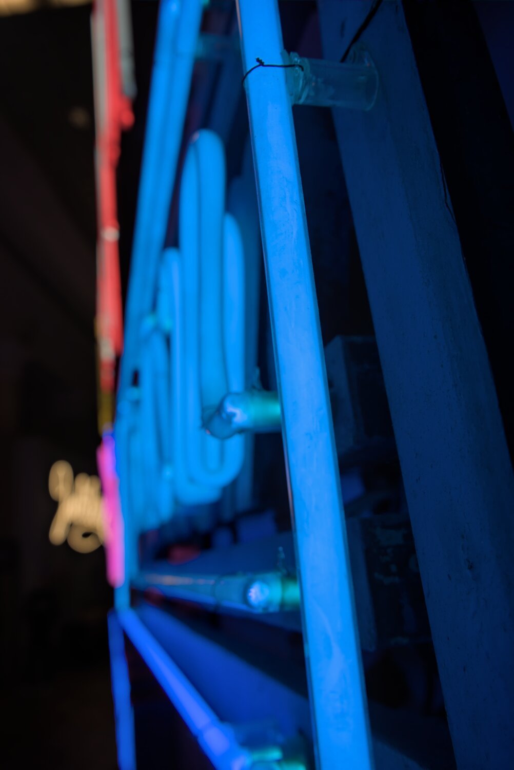 a singular blue stripe of neon in focus, with pink, red and yellow signs in the background
