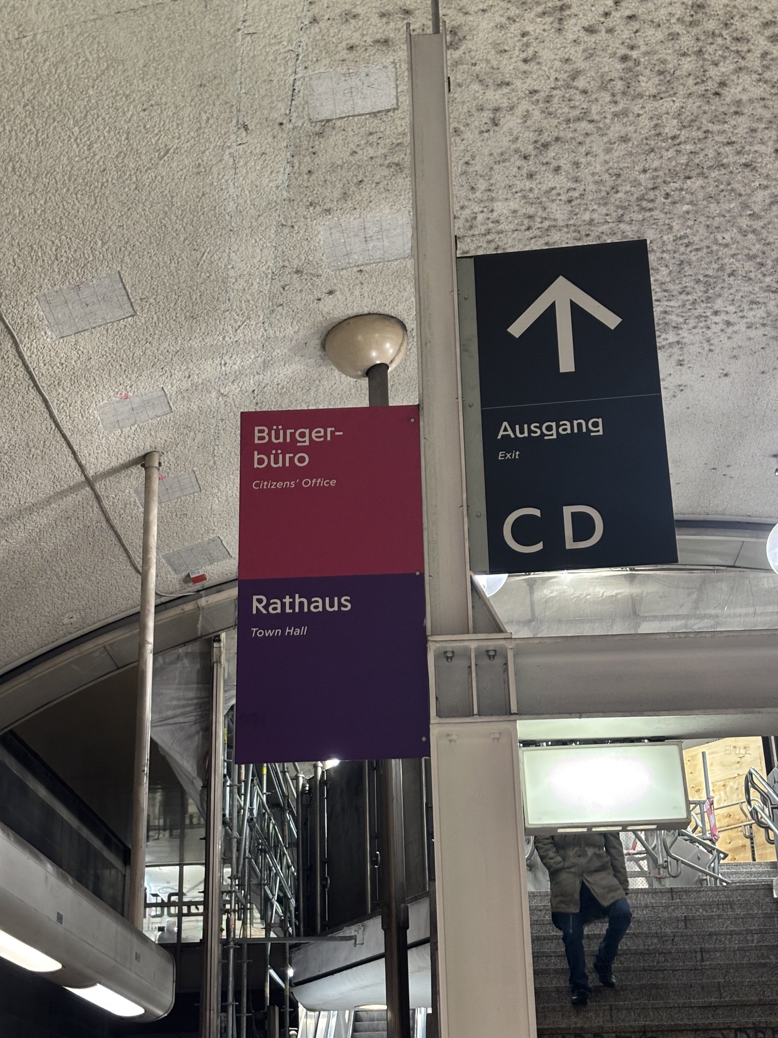 a train station exit with signs for 'Bürger-büro' (Citizens' Office) and 'Rathaus' (Town Hall) in purple and pink respectively... The font on the exit sign is quite angular and modern looking
