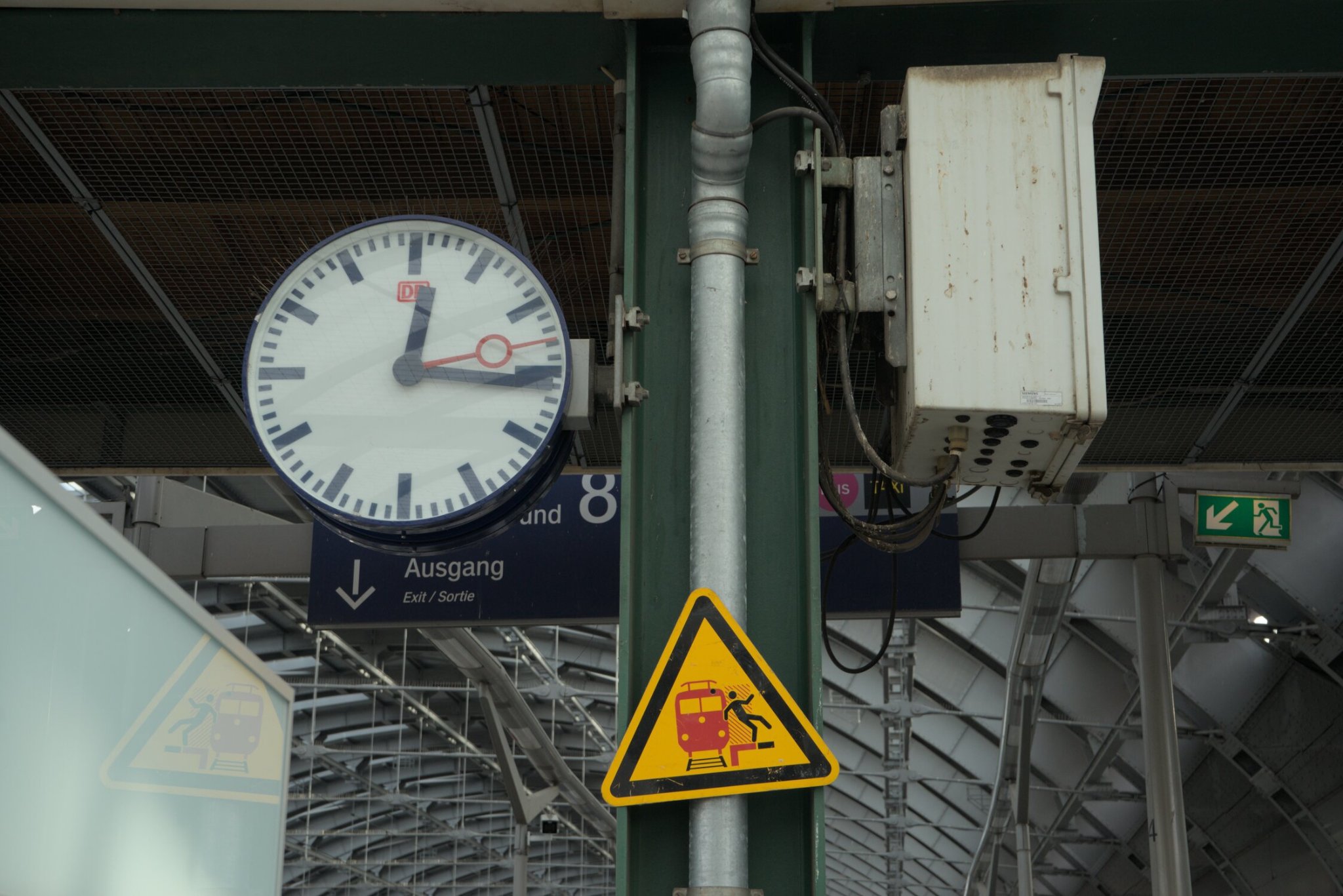 a DB clock saying 12:16 and a tilted caution sign warning to be careful around the tracks