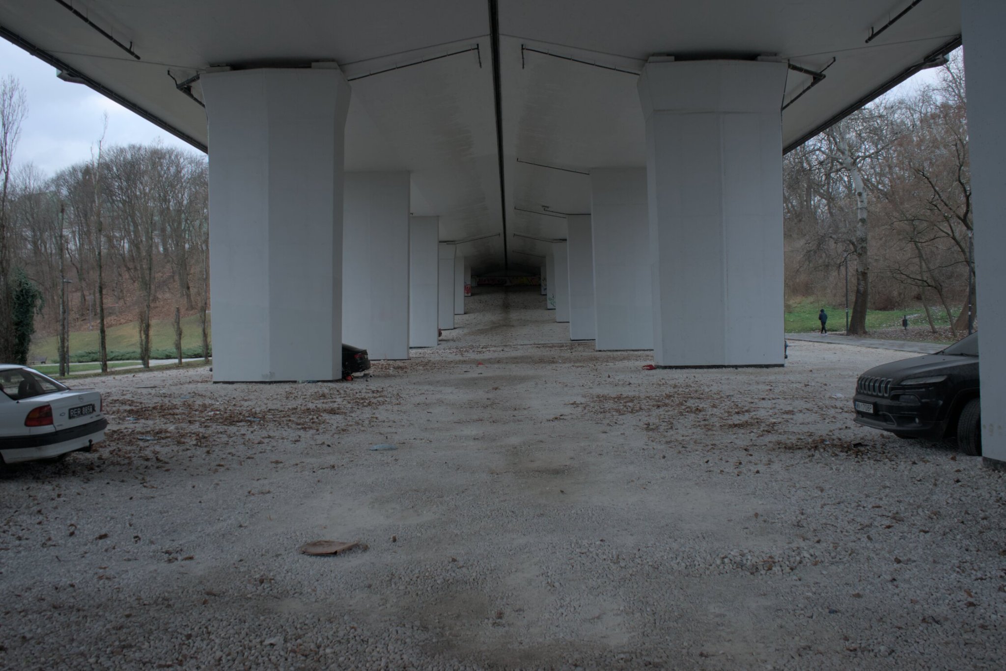 the underside of a highway overpass, cars parked on the sides, towards the background looks quite ominous...