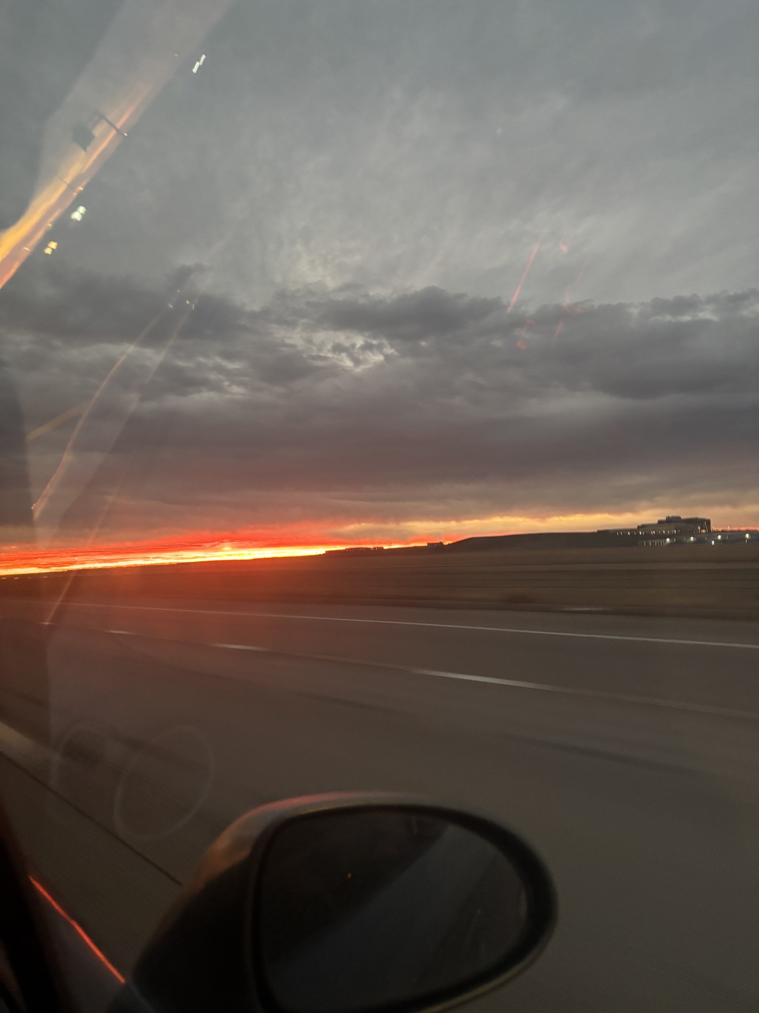 making my way to the airport, reflections of the car's window visible, the sun is rising and the highway lines are blurry