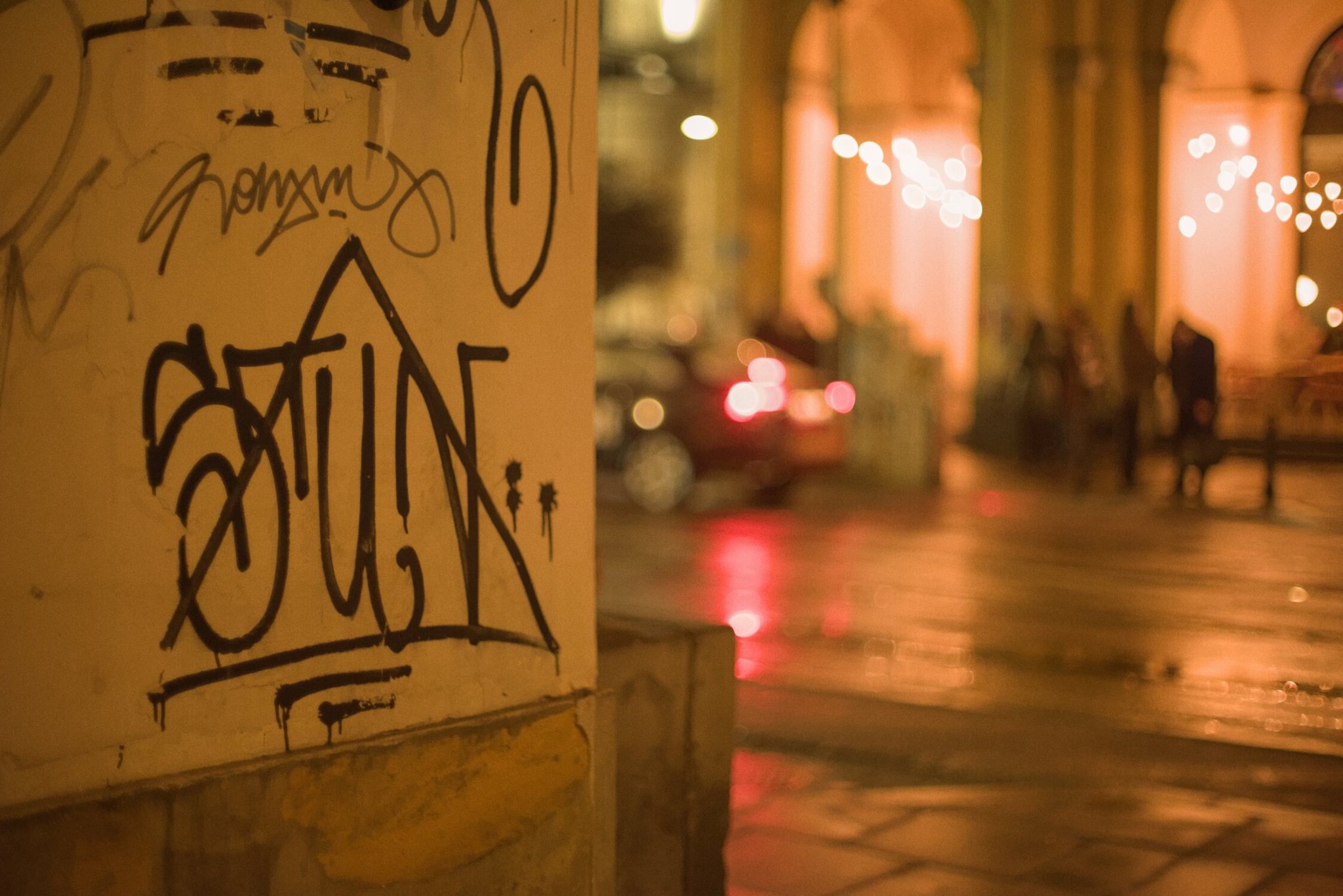 some grafitti, filling the left of frame, looking out onto the street beyond, blurry though it may be, it is apparent that it's still somewhat wet from a recent rainfall