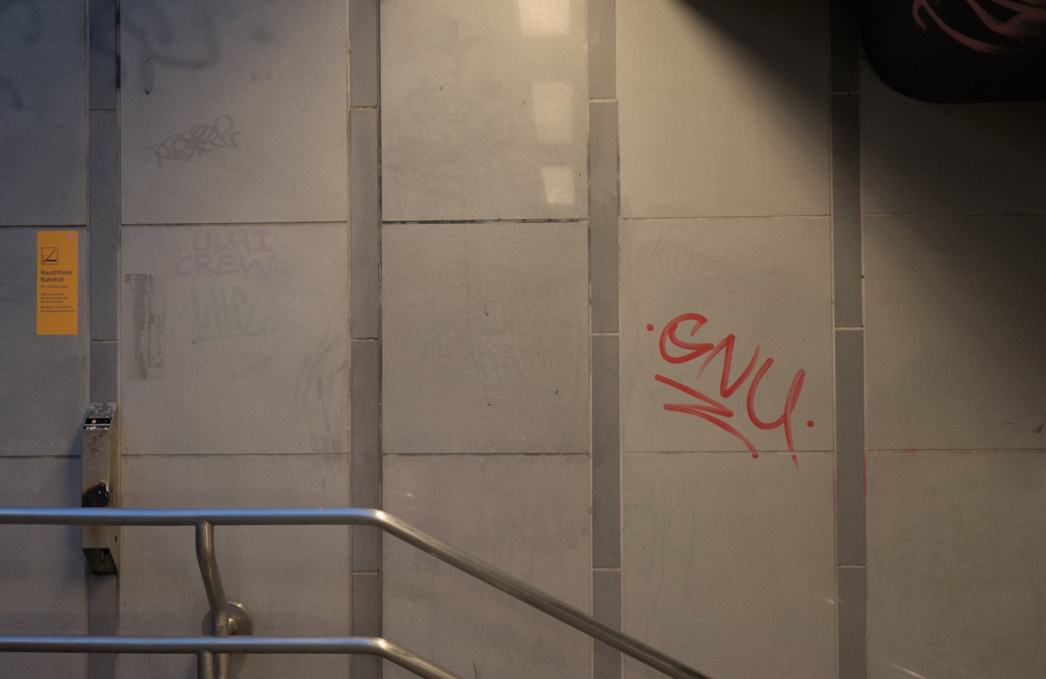 a stairway's handrail, on the far left is a blurry yellow placard with the essense of the message being 'no smoking', and towards the right of the frame is some grafitti that says 'GNU' (whether in relation to the GNU project, i have no idea, but probably not)