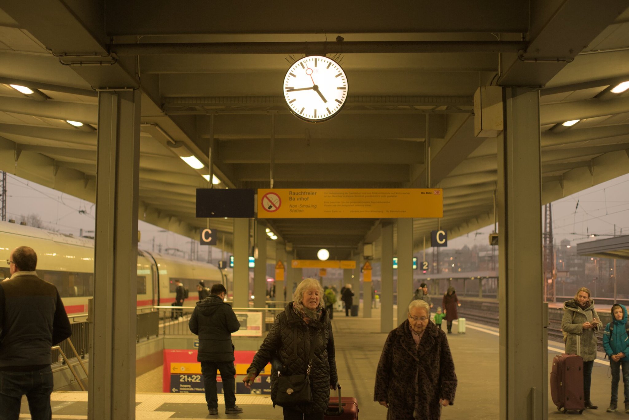 a DB clock is the focus here, reading 4:43, a no smoking sign in the background, with passengers abound, waiting for their train or perhaps moving to their connection point... there is an ICE train waiting on platform one, to the left