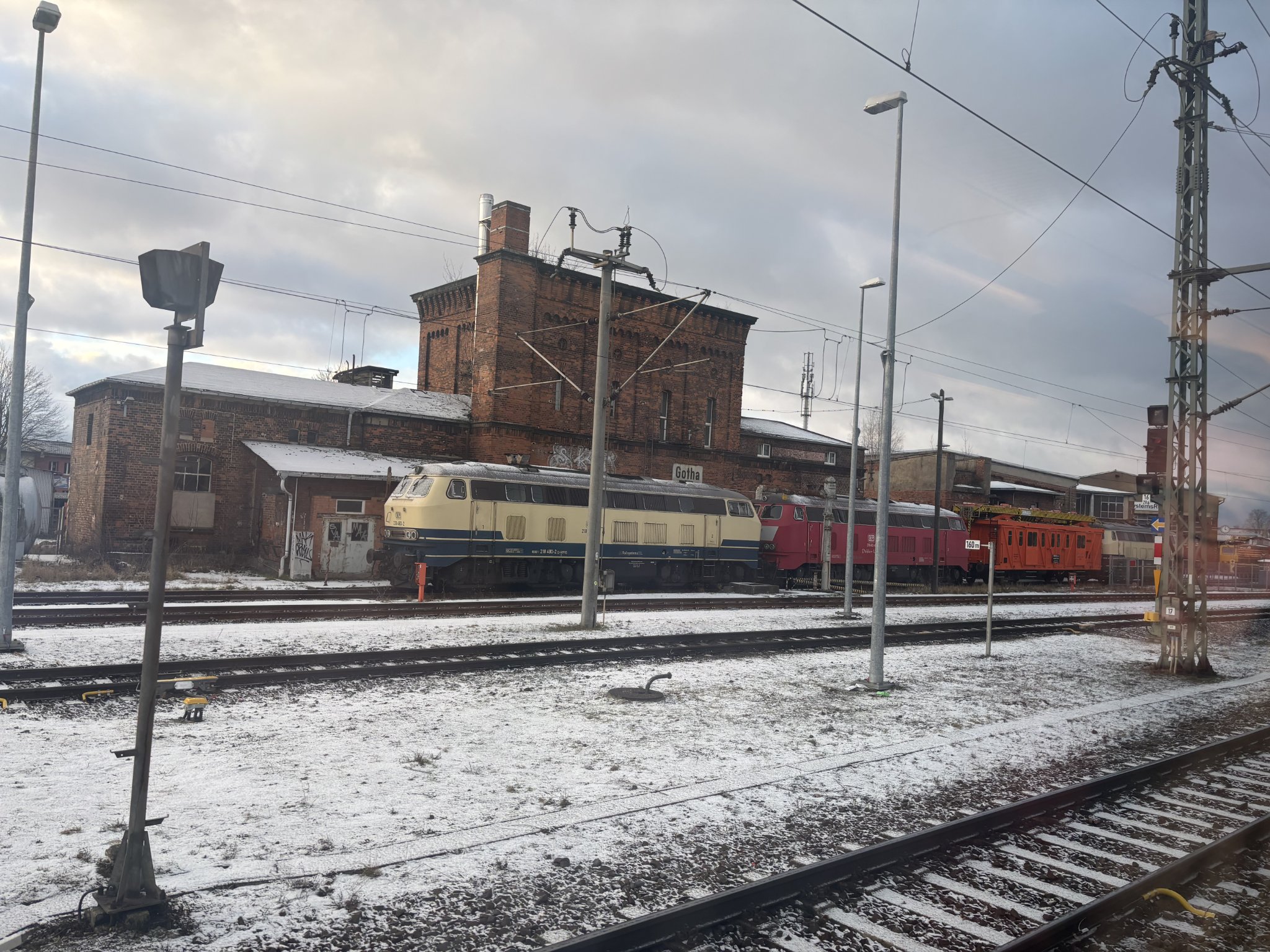 some older rolling stock, positioned next to an old factory building, three tracks between the viewer and the subject