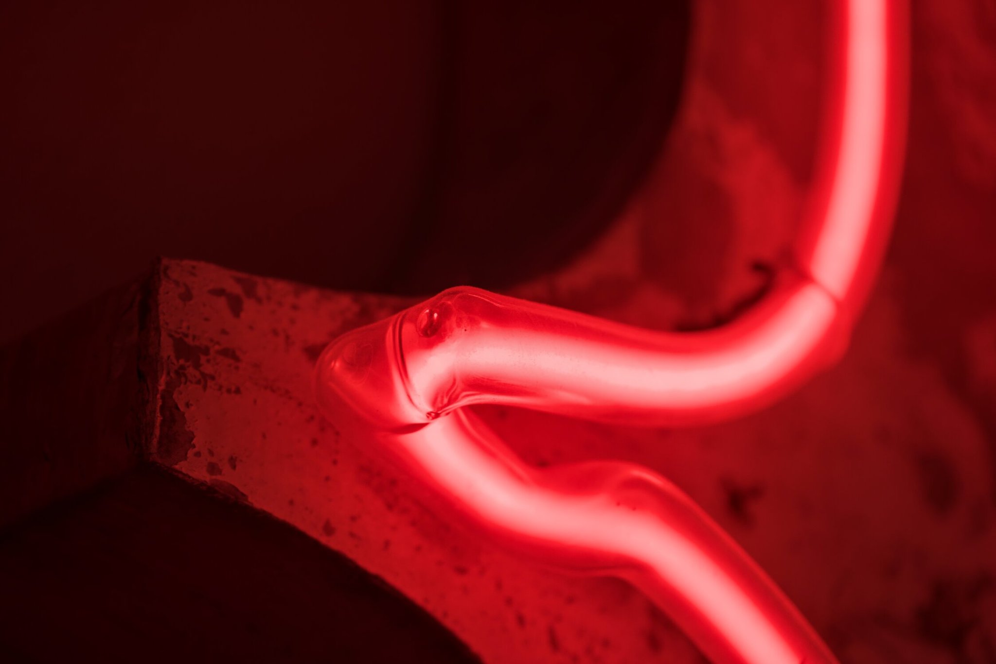 a red curve of neon, the gap between the glass and plasma visible, attached to a worn backing