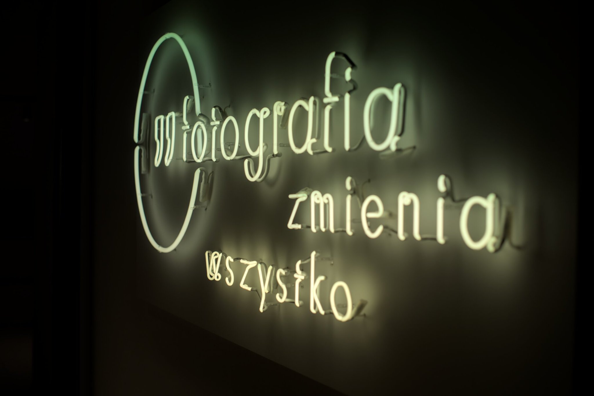a neon sign reading 'fotografia zmienia wszystko', its color fading from green at the top to a creamy white at the bottom (no idea why that happened, i didn't edit it to be like that)