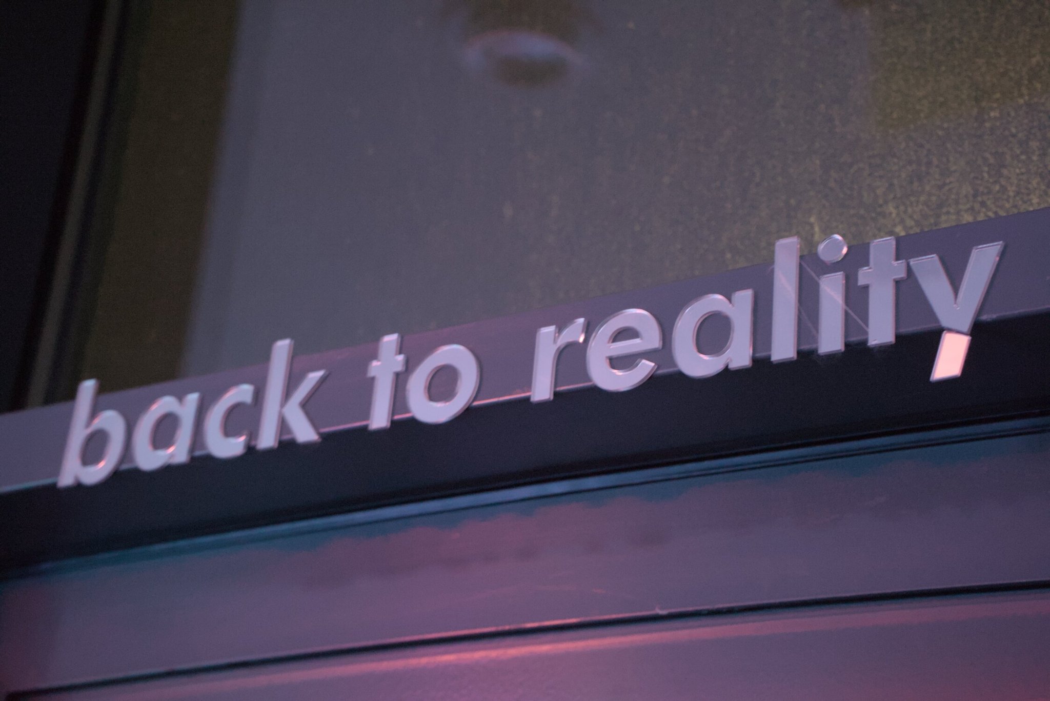 a mirrored exit sign, saying 'back to reality' in a modern font, the 'y' having its tail broken