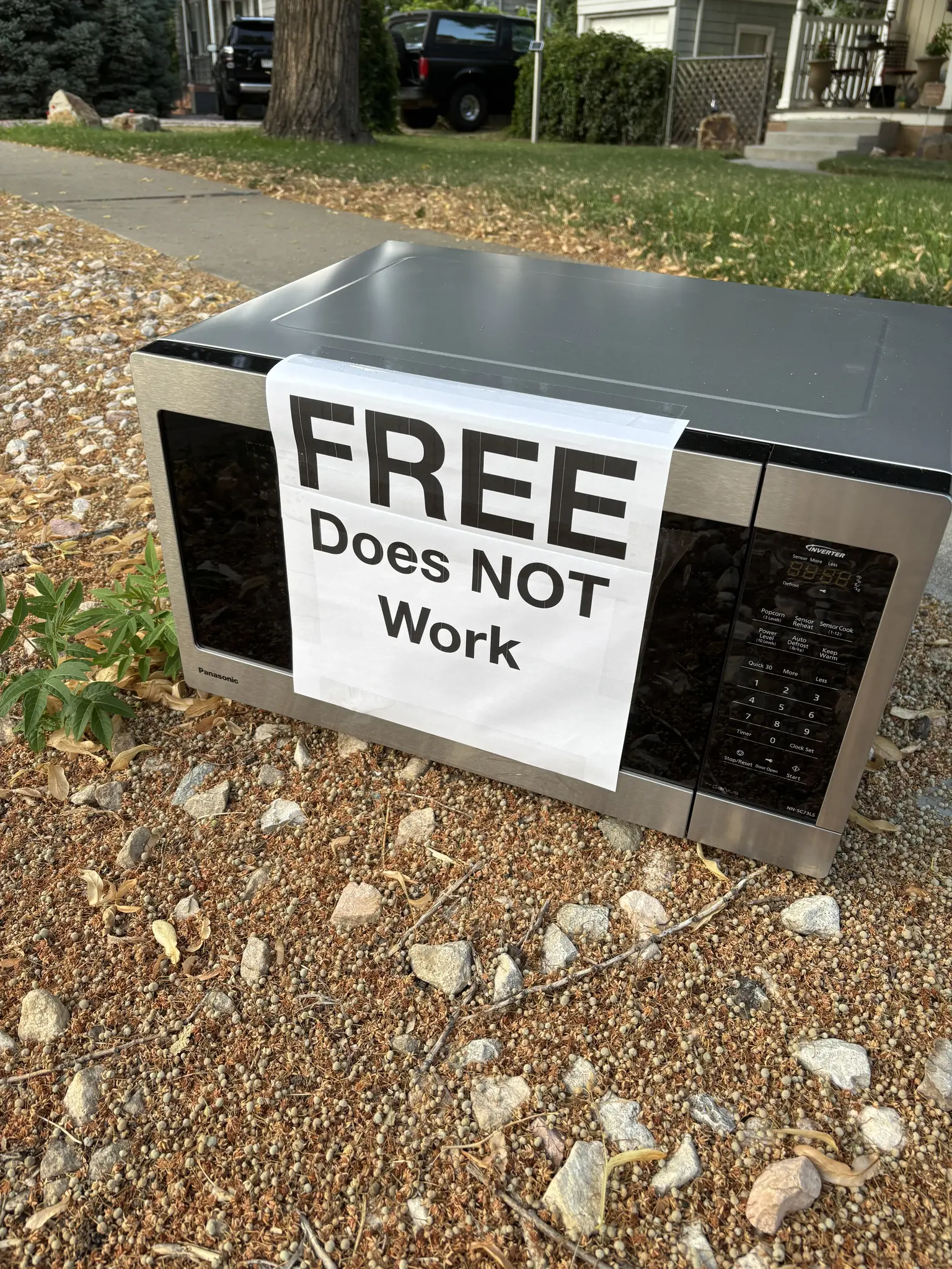 a microwave abandoned to the side of the road with a sign that says "free - does not work" attached