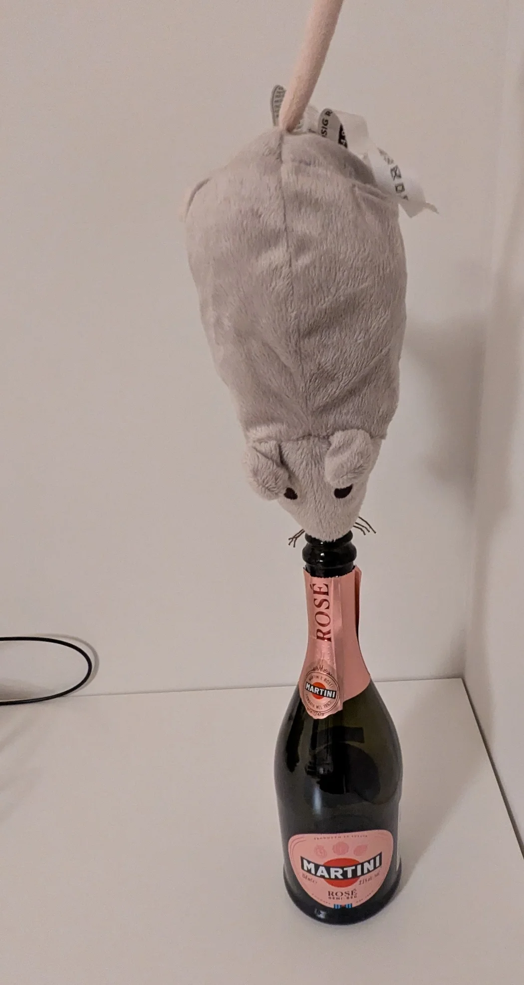 an ikea rat with its nose inside of a bottle of sparkling wine