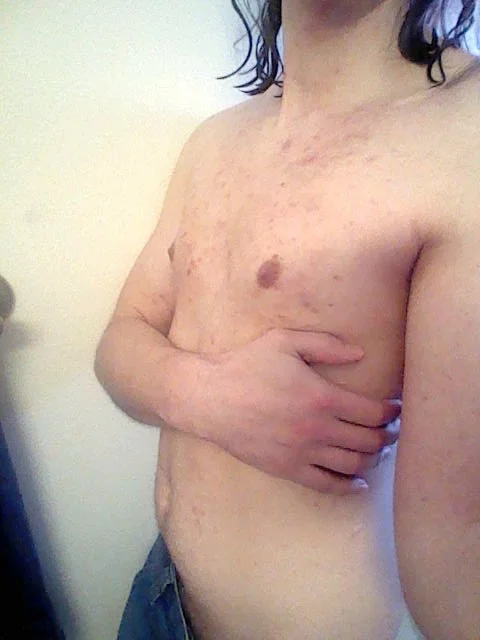 me, standing in front of a white wall, arm across my  bare chest, jeans visible towards the bottom of the shot
the photo is rather crunchy and low resolution, having an almost dreamy, mid 00s mood to it