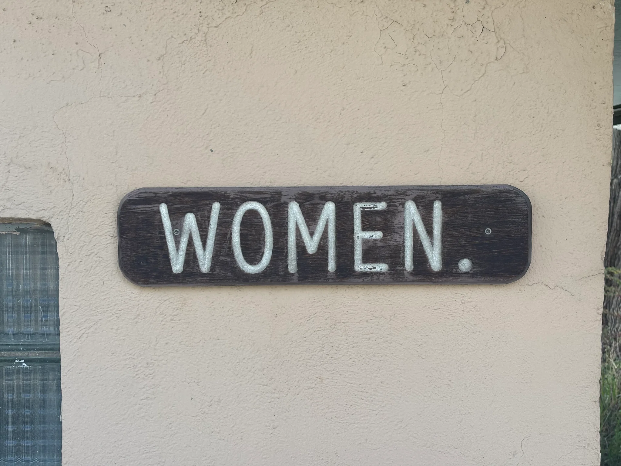a wooden sign that has "women." painted upon it