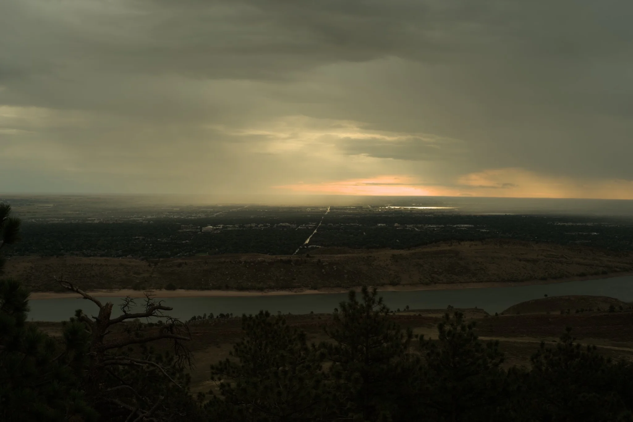 we look over horsetooth reservoir, the sun has risen, it sits beyond the rain, reflecting upon the lake, so far in the distance, the pines wait in anticipation for the warm sun to grace their needles