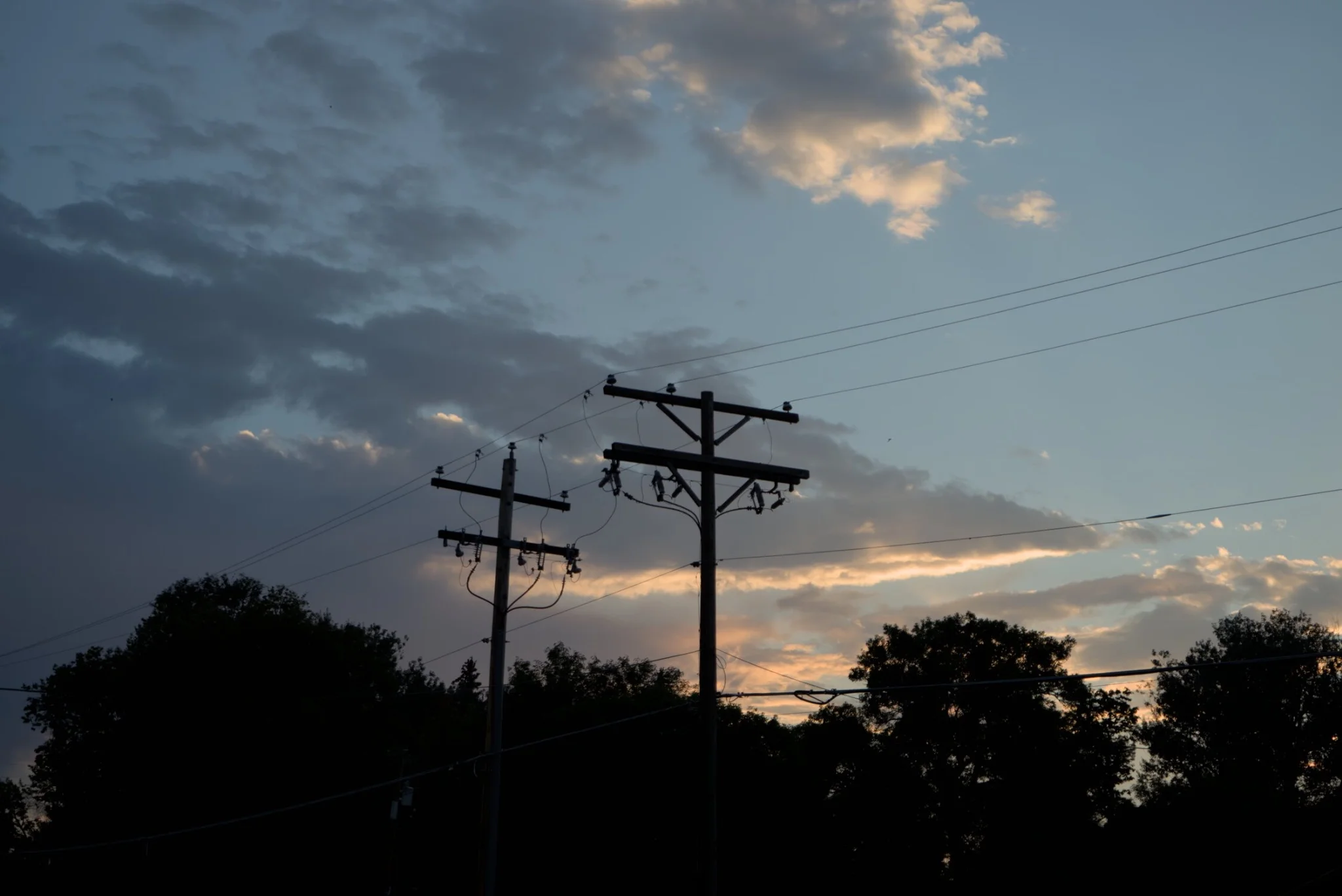 a silhouette of power poles and trees, in front of an sunset, partly cloudy sky