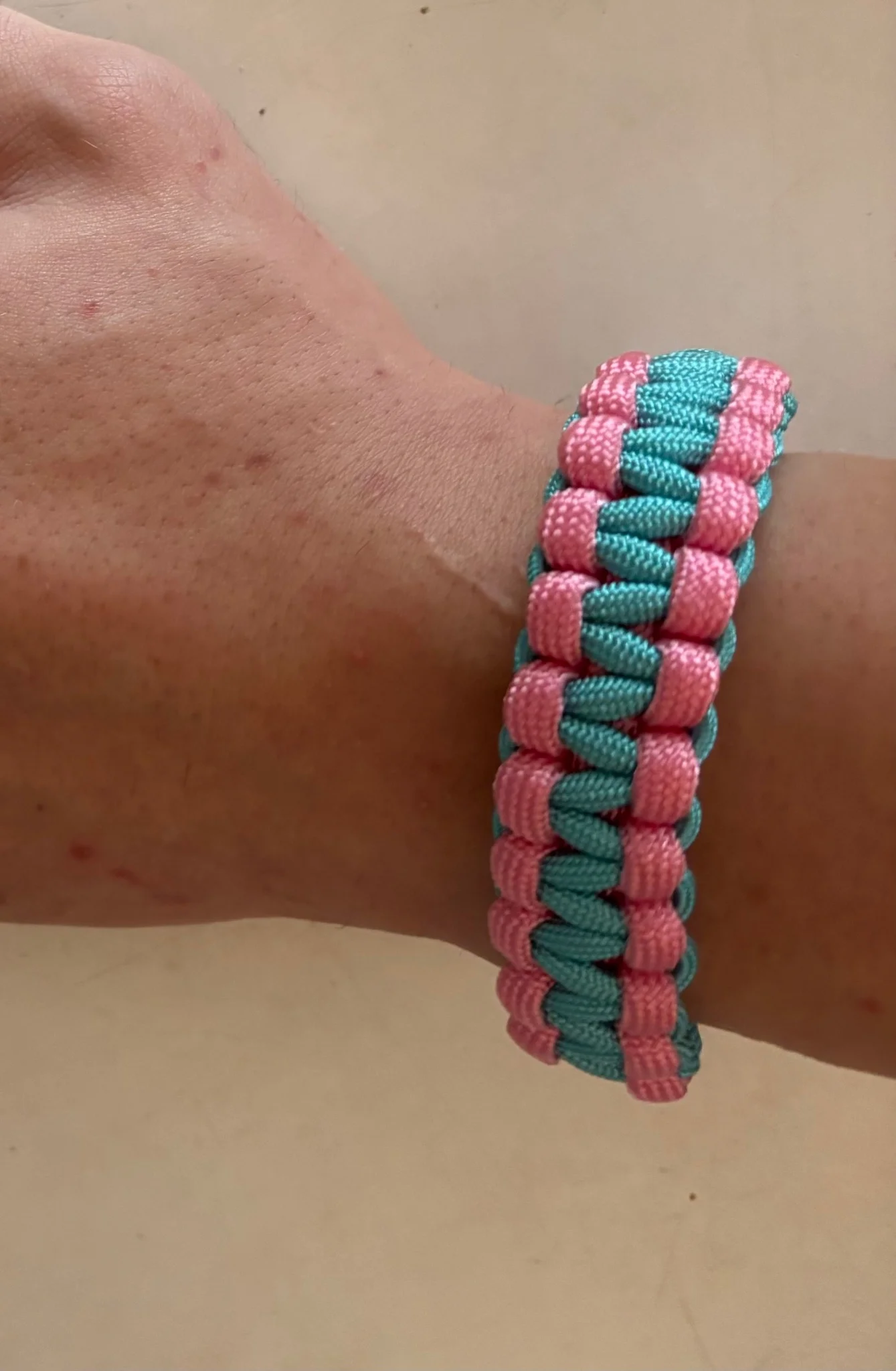 a pink and blue paracord bracelet, being worn on my wrist, the weave is the standard cobra design, with the pink being the outer part and blue being the inner