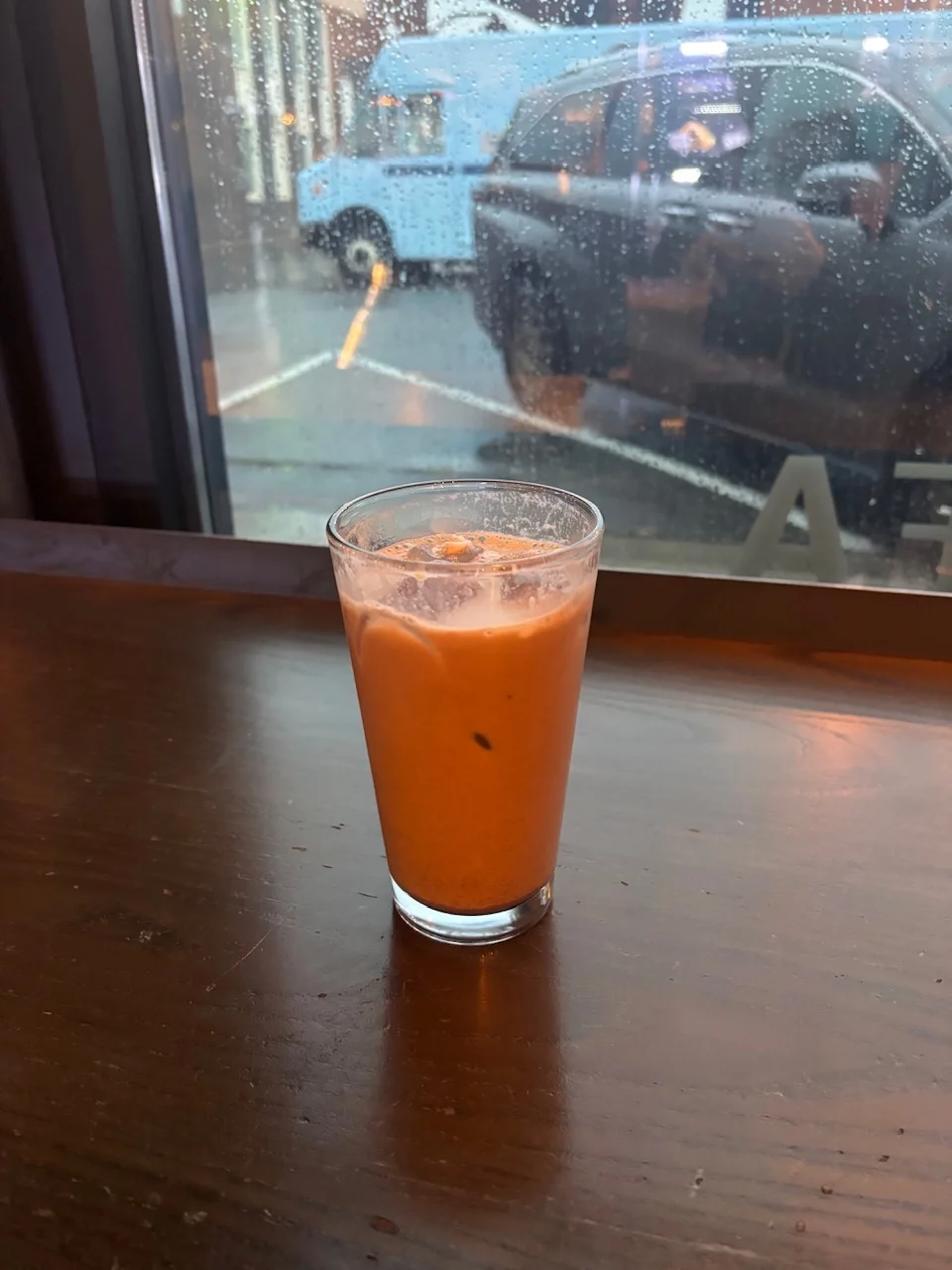 an iced mocha latte, behind which is a rain slicked window, looking out onto the street where cars rest
in the reflection of the window, the coffee bar and i can vaguely be seen