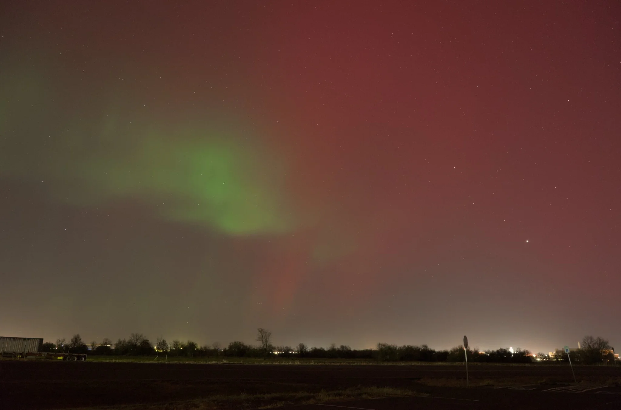 red and green aurora, with plenty of light pollution on the horizon