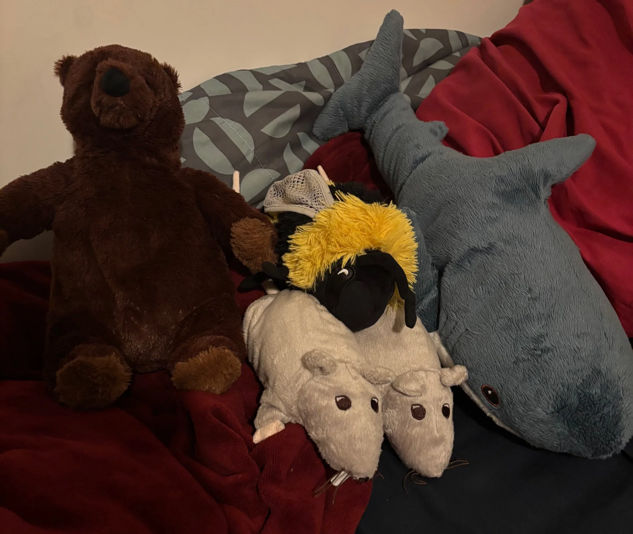 a bear, bee, shark and two rat plushies pose for a picture whilst sitting atop blankets and pillows