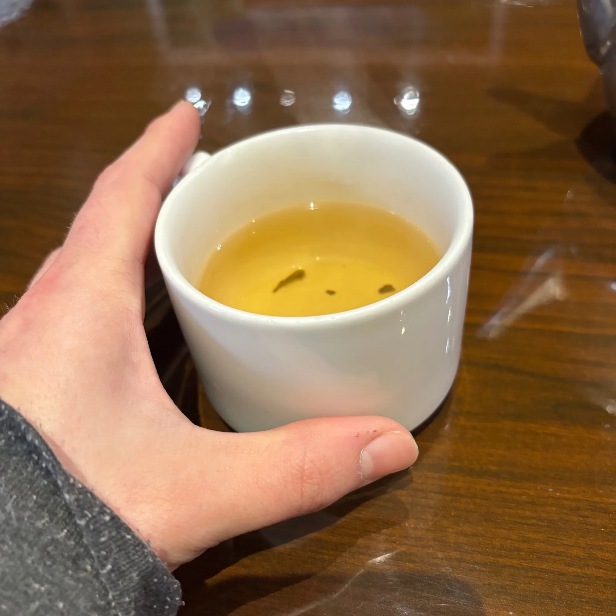 a cup of jasmine tea with leafy bits floating within, beside it is tidy's hand
