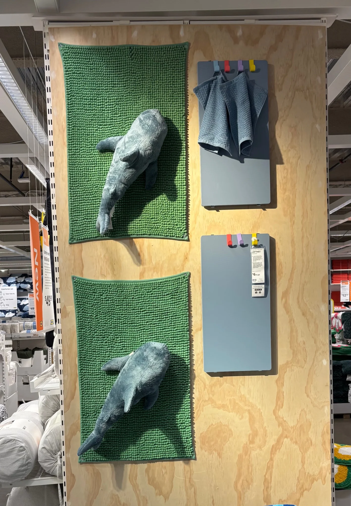 a couple of small blahaj attached to bath mats that are attached to a wall in ikea for some reason