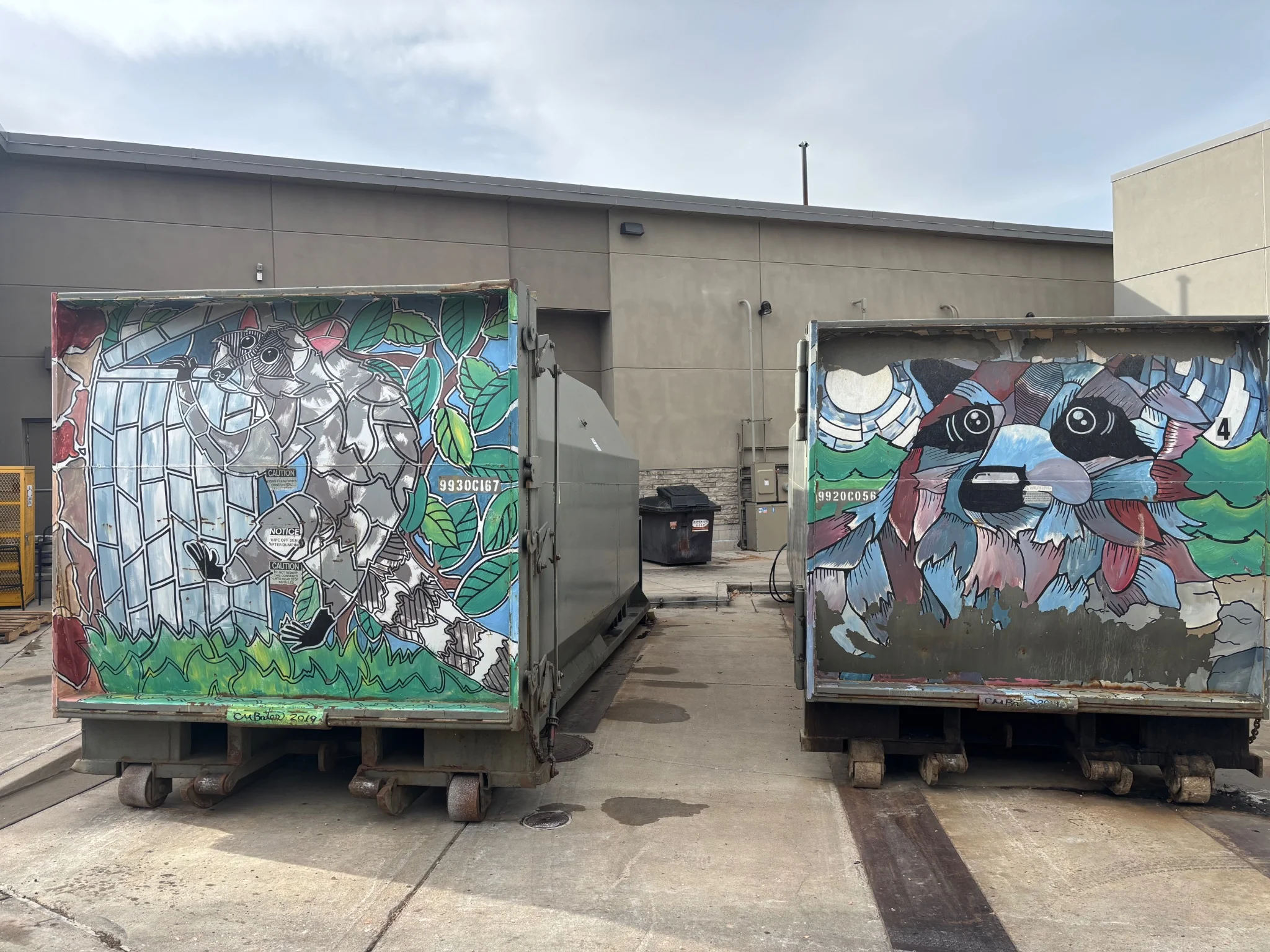 a pair of industrial size dumpsters with abstract raccoon themed artwork