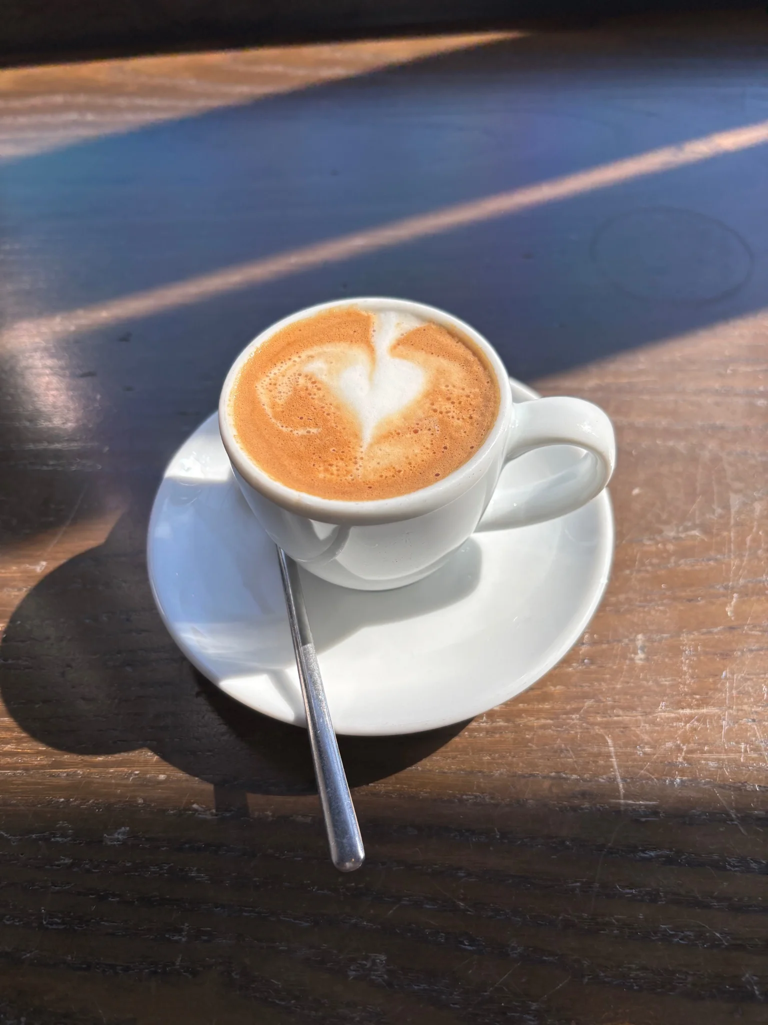 a macchiato, basically an espresso with a drizzle of milk in it
the sun is beaming in from the upper left, and the milk in the coffee makes a vague heart shape