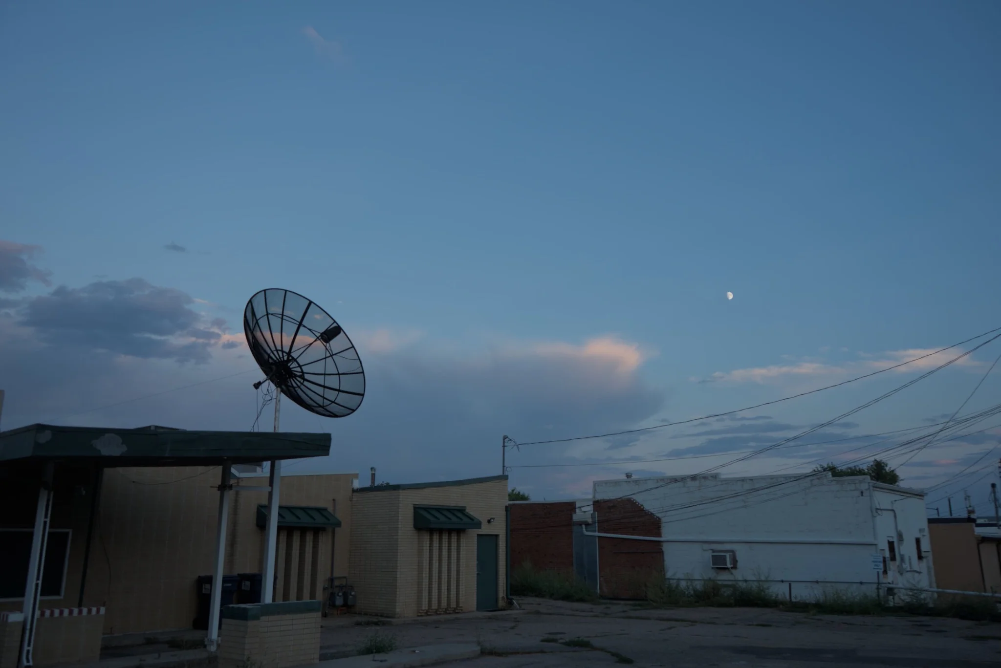 a satellite dish, sitting atop a building, looking somewhat like it's pointed at the moon
a parking lot and buildings are visible in the foreground