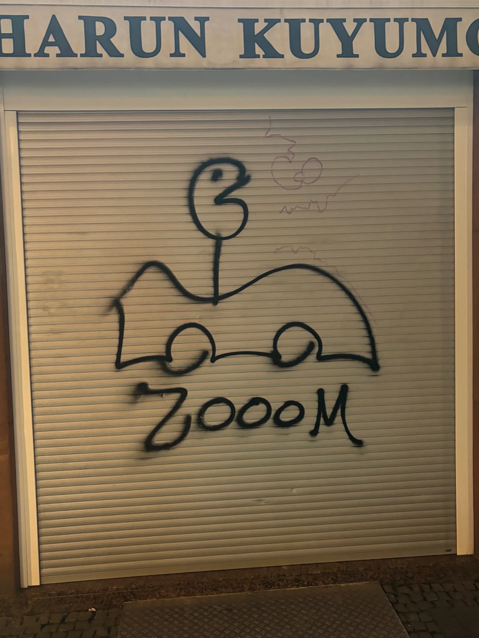 a stick figure with a pacman looking head in a car with the text below reading "zooom", all of this being emblazoned on a garage door of sorts, in spray paint