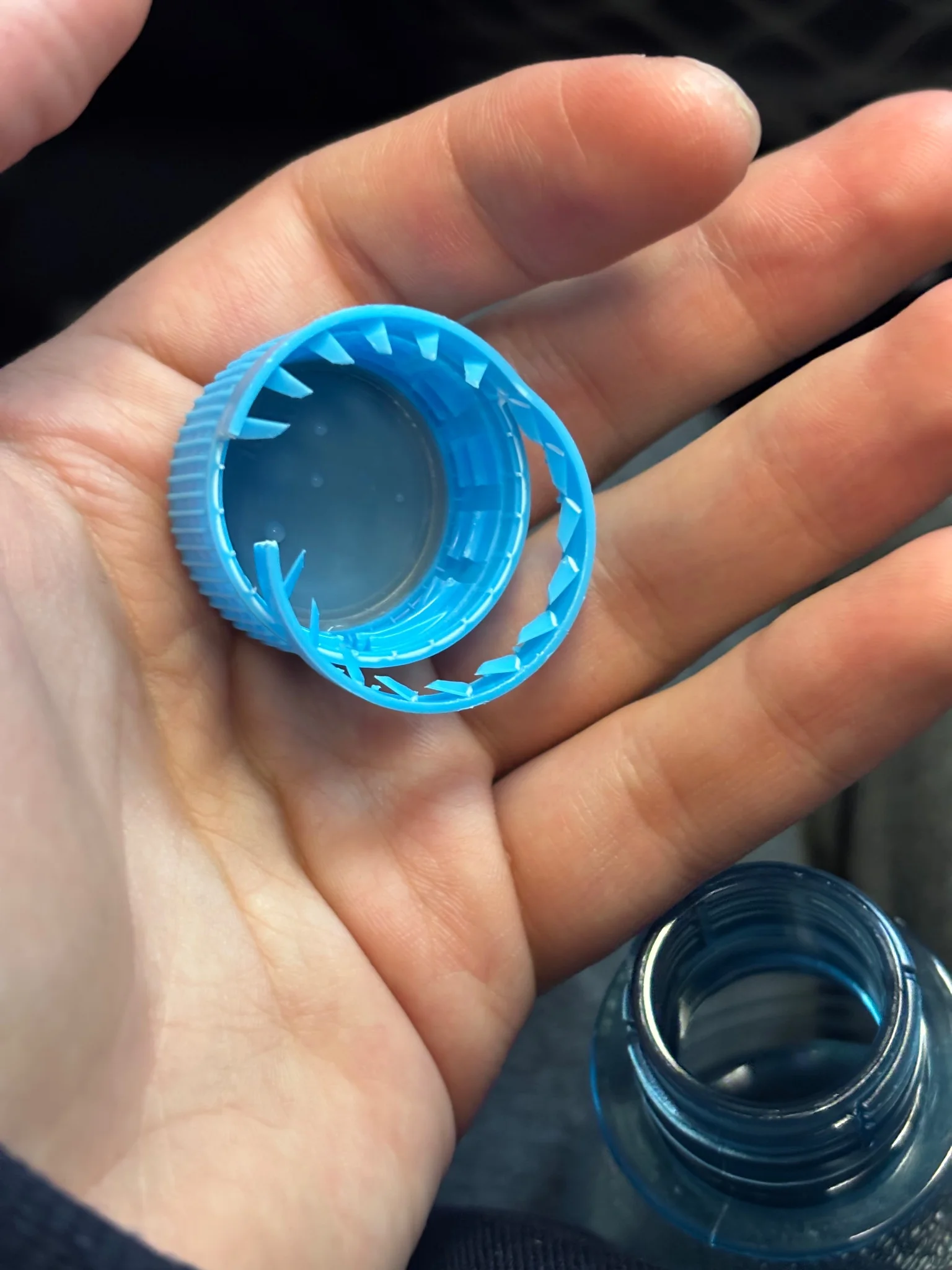 me holding a water bottle cap in my left hand, the retaining ring snapped incorrectly, completely removed from the bottle between my legs