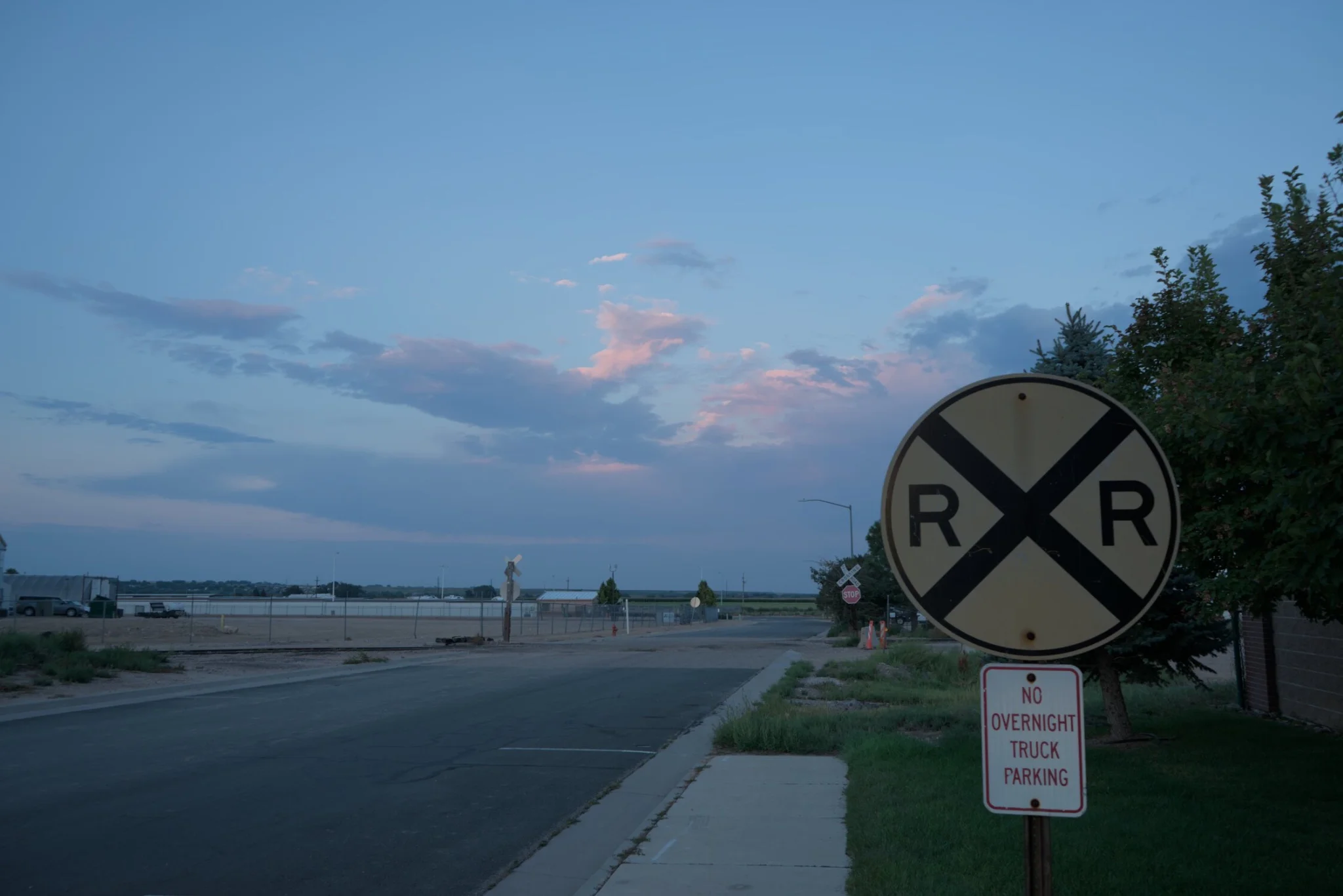 a railroad crossing sign, with a 'no overnight truck parking' sign below it, all in front of a sunset partly cloudy sky