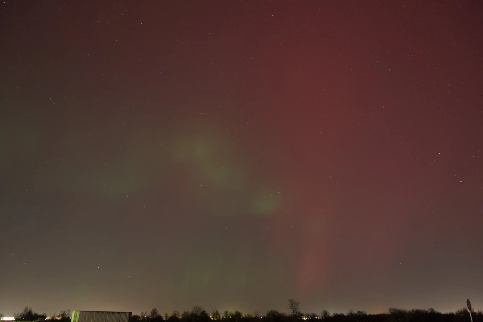 more red and green aurora, with a light polluted horizon, the stars peeking through